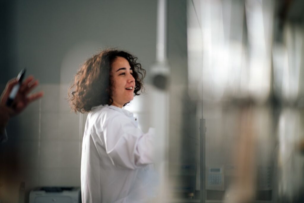 A young female scientist with curly hair in a lab coat working in a laboratory setting.